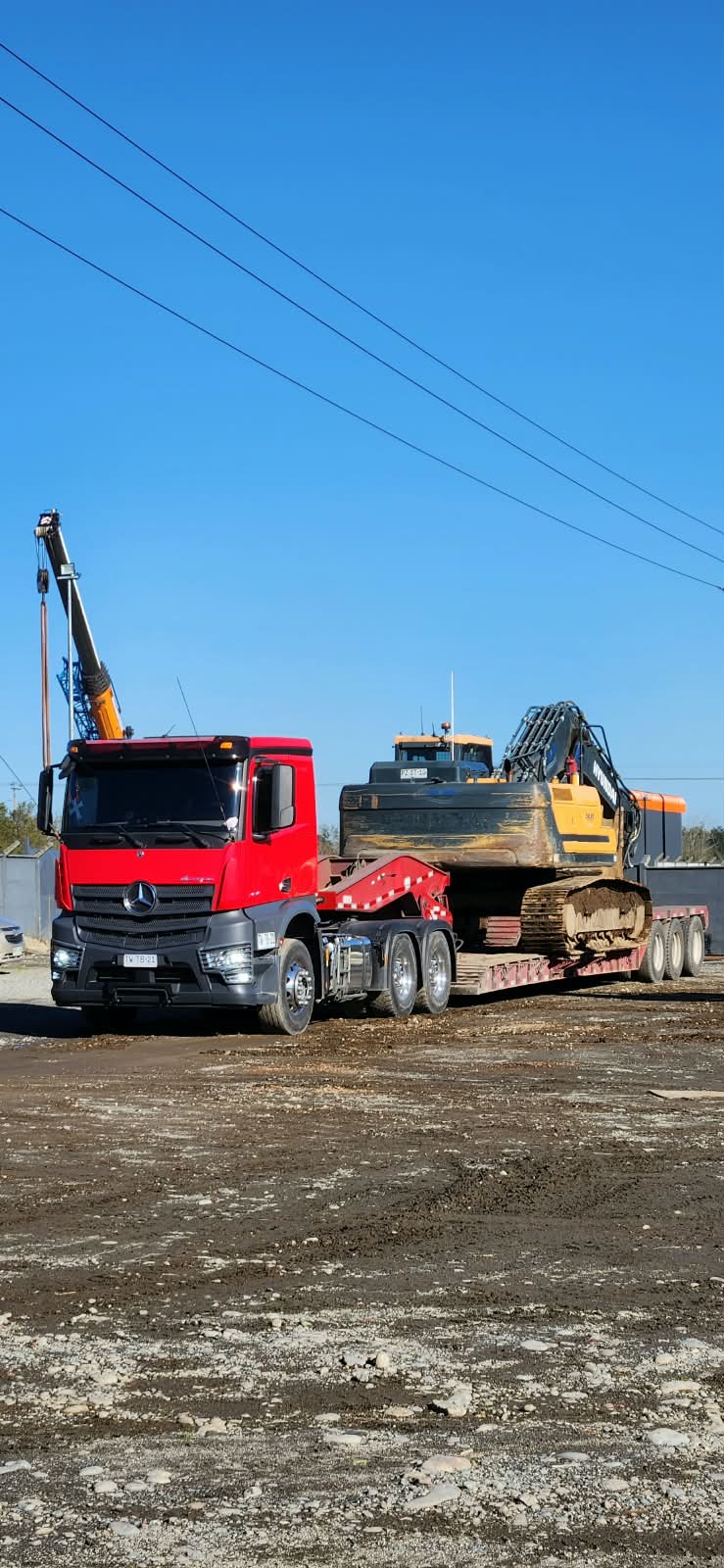 Camión con grúa transportando excavadora en cama baja