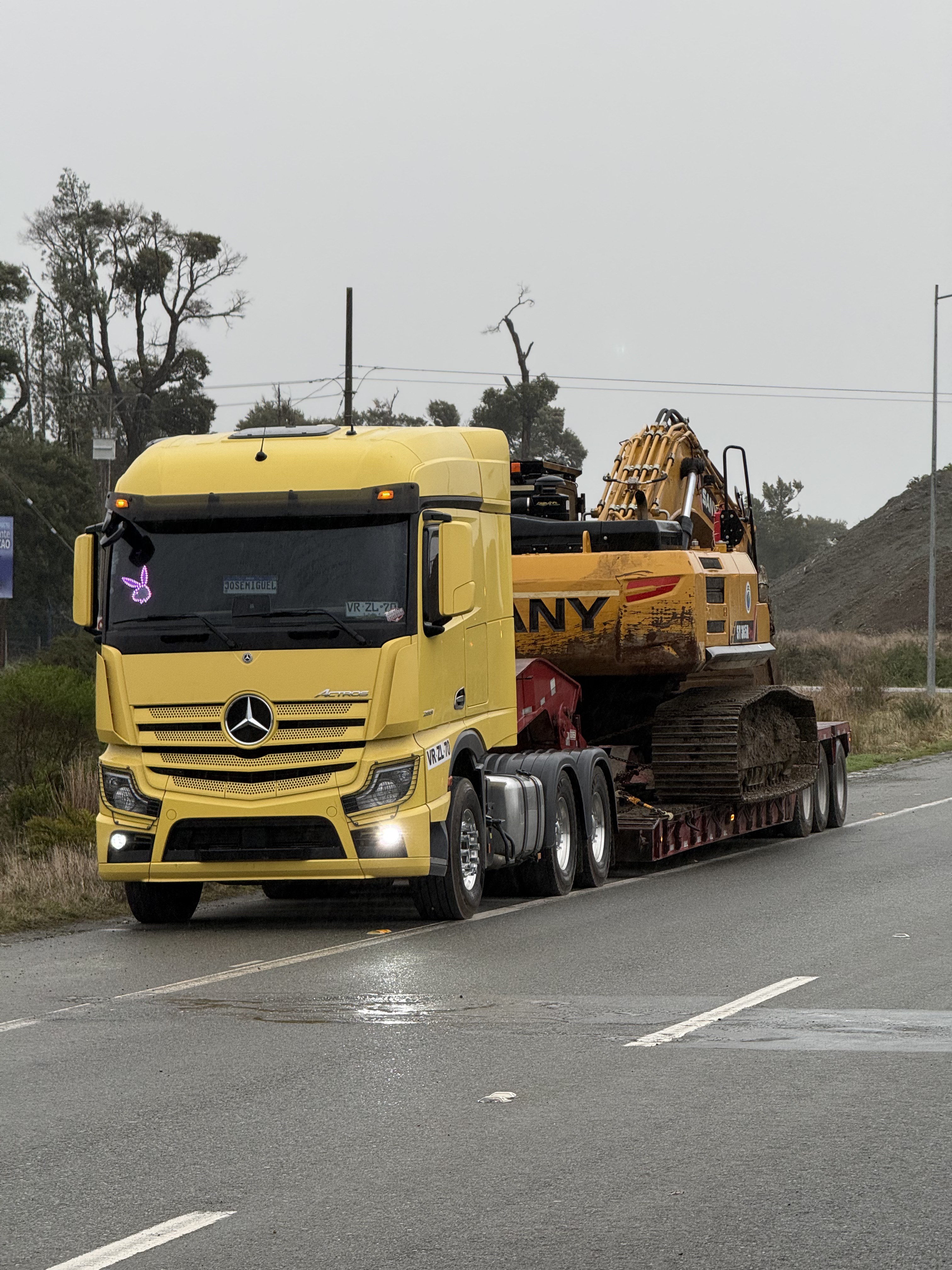 Camión cama baja amarillo de Transportes Flores trasladando excavadora