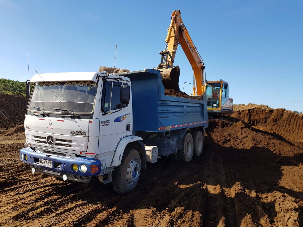 Excavadora cargando tierra en camión tolva en faena de Transportes Flores